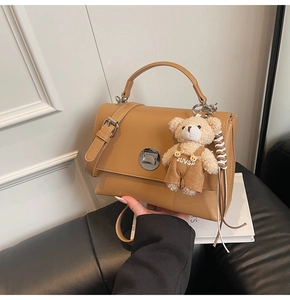 Detail view of khaki crossbody bag with silver twist lock and plush bear charm