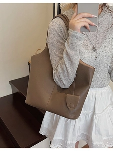 Dark brown leather bucket tote bag with leaf pendant charm shown in a model mirror selfie
