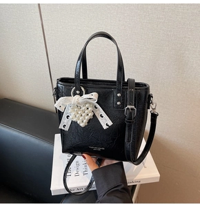 Détail du sac seau noir en cuir brillant avec pendentif cœur perlé et nœud dentelle