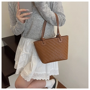 Detailed close-up of brown woven faux leather tote bag with knot handle detail on model