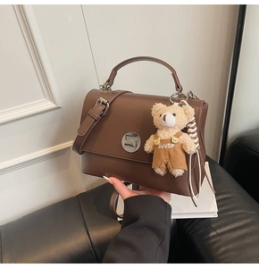 Detail of dark brown leather satchel featuring a gold swivel lock and a plush bear charm