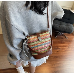 Detail view of woven bucket bag with multi-color stripes and brown leather strap on model