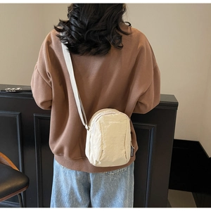 Détail du sac bandoulière en nylon beige avec broderie et bandoulière réglable