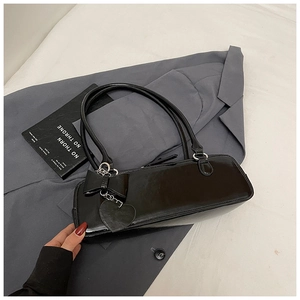 Detail of black patent leather baguette bag with bow and heart charm on grey blazer