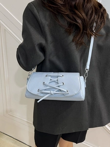 Chic light blue leather shoulder bag with cross-lace detail and silver hardware worn on a suit