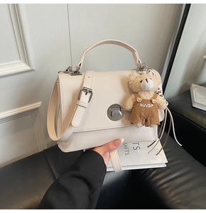 Detail of off-white crossbody bag with silver twist lock and cute teddy bear charm