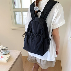 Close-up of black nylon backpack featuring functional drawstring pockets and side buckles