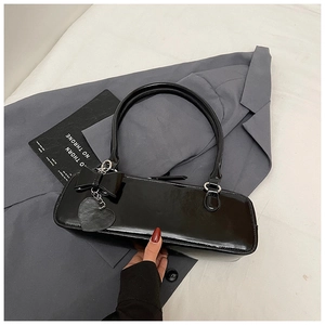 Detail of black glossy baguette bag with heart pendant on a grey suit jacket