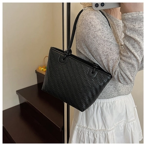 Side view of model wearing a black woven tote bag made of soft faux leather