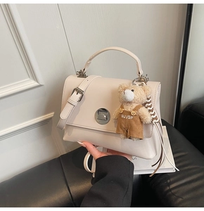 Detail of a creamy white crossbody bag with silver twist lock and cute teddy bear charm