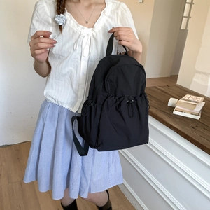 Detail of a black nylon backpack with side drawstring pocket and durable top handle