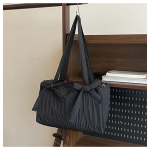 Detail view of black pleated nylon tote bag featuring decorative bow accents on the strap