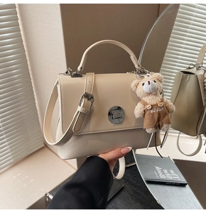 Detail of a cream faux leather crossbody bag with a metal twist lock and cute bear charm