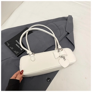 Detail view of a white leather baguette bag with a bow accent and heart pendant