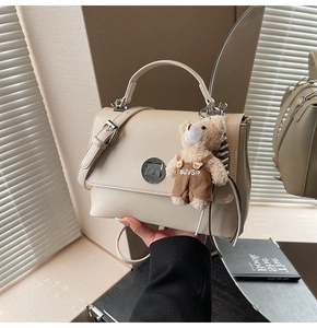 Detail of cream flap crossbody bag with metal lock and cute teddy bear pendant charm