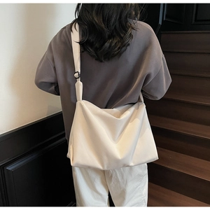 Rear view of a model wearing a large cream canvas crossbody bag on a wooden staircase