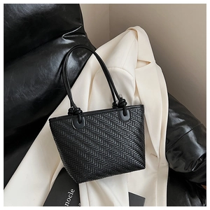 Close-up of black woven tote bag with unique knot detail handles on white suit background