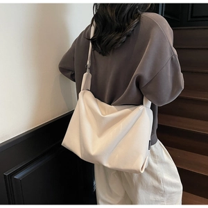 Close-up of a large off-white crossbody bag featuring a wide strap and minimalist style