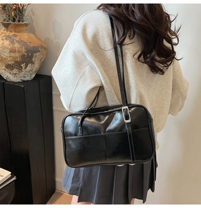 Detail van zwarte waxleren schoudertas met zilveren gesp, gedragen door een model in casual stijl