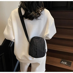 Détail d'un sac bandoulière en nylon noir avec large sangle porté par un mannequin