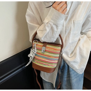 Detail of colorful woven straw bucket bag with brown leather trim and silver dinosaur charm