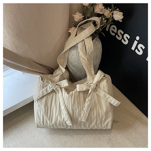 Close-up of beige pleated nylon bucket bag featuring decorative ribbon bows and soft texture