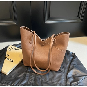 Detailed view of brown textured leather tote bag with magnetic clasp on dark wood background