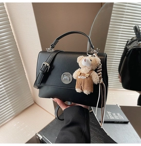 Detail of black crossbody bag with silver twist lock and a cute teddy bear charm