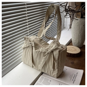 Detail of beige pleated nylon shoulder bag with dual ribbons on a sunny window sill