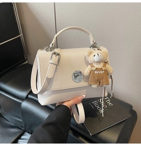 Detail of a creamy white PU leather handbag with metal turn-lock and plush bear charm