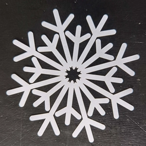 Detailed top view of white snowflake cutout coaster on a textured black surface