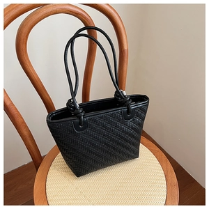 Close-up of black woven leather tote bag texture on a vintage wooden chair