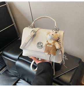 Detail of creamy white crossbody bag with silver twist lock and plush bear charm