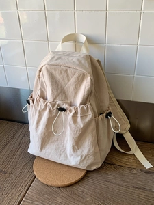 Minimalist beige nylon backpack featuring side drawstring pockets and durable top handle