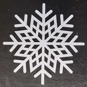 Detail view of laser-cut white snowflake coaster with geometric patterns on black surface
