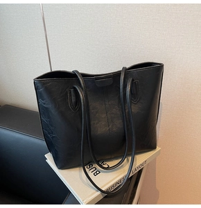 Detail of black leather tote bag with long handles and buckle resting on a sofa