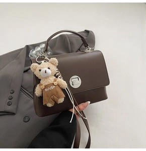 Close-up of retro brown leather handbag featuring silver clasp and cute plush bear charm