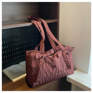 Detail of dark mahogany pleated nylon tote bag with dual decorative bows on a bookshelf
