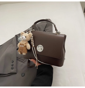 Detail of a dark brown structured satchel bag with plush bear charm and metal buckle