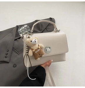 Detail of cream crossbody bag with round metal buckle and plush bear pendant detail