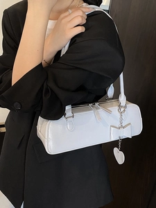 White baguette shoulder bag with bow and heart charm on black suit background