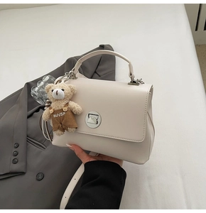 Detail of cream crossbody bag with metal twist lock and cute brown bear pendant charm