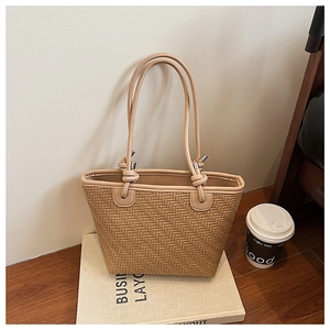 Detail of beige woven bucket bag with herringbone texture and knotted strap accents