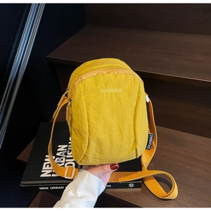 Détail d'un sac bandoulière en nylon jaune vif avec fermetures éclair multicouches sur bois