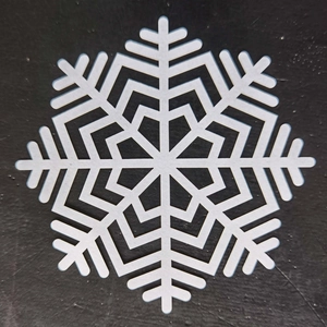 Top view of laser-cut white snowflake coaster with geometric pattern on black surface