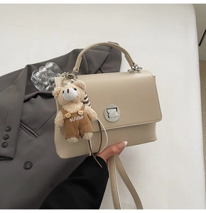 Detailed close-up of beige leather handbag with metal lock and cute plush bear charm