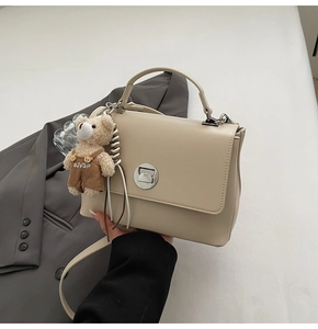 Detail of beige satchel bag with silver clasp and cute plush bear charm accessory