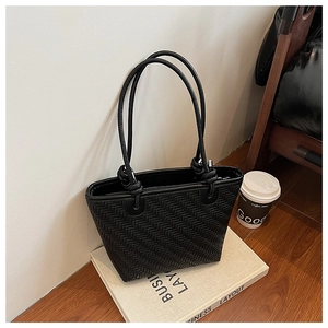 Detail of black woven texture bucket bag with knotted rope handle on business book