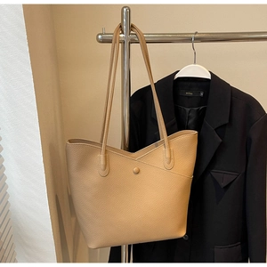 Detail of beige pebbled leather tote bag hanging on hanger with a black blazer backdrop