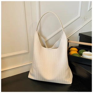 Detailansicht der cremefarbenen gewebten Hobo-Tasche auf einer schwarzen Stufe mit Tee